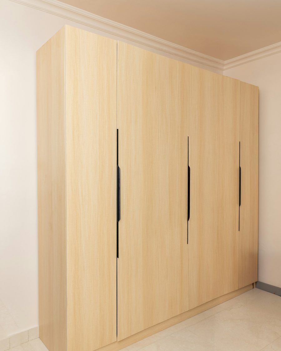 Raumhoher Einbauschrank in heller Esche mit vier Türen und eingefrästen schwarzen Griffleisten in einem hellen Zimmer